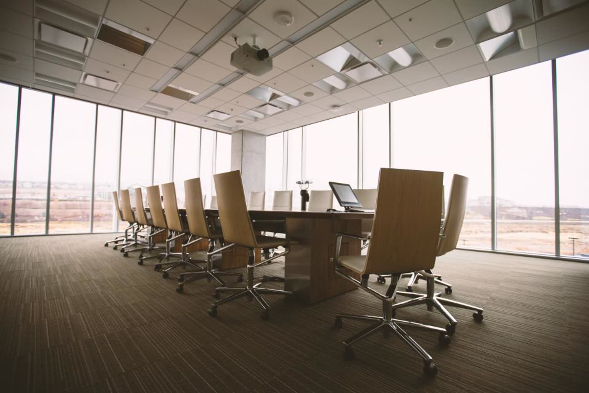 A long boardroom table with leather chairs facing tall windows