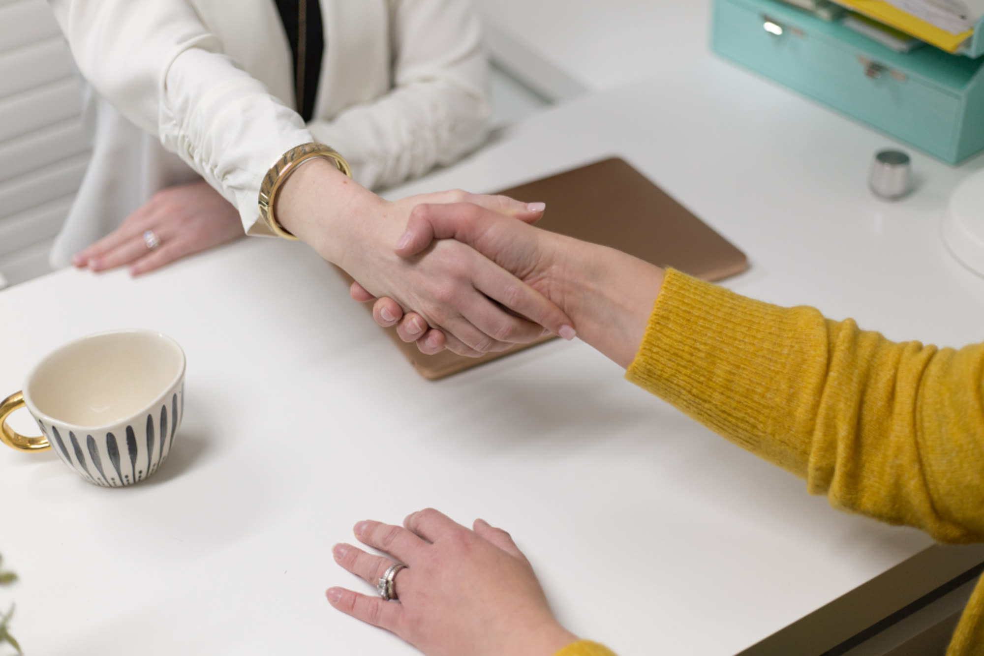 Two people shaking hands over a white desk