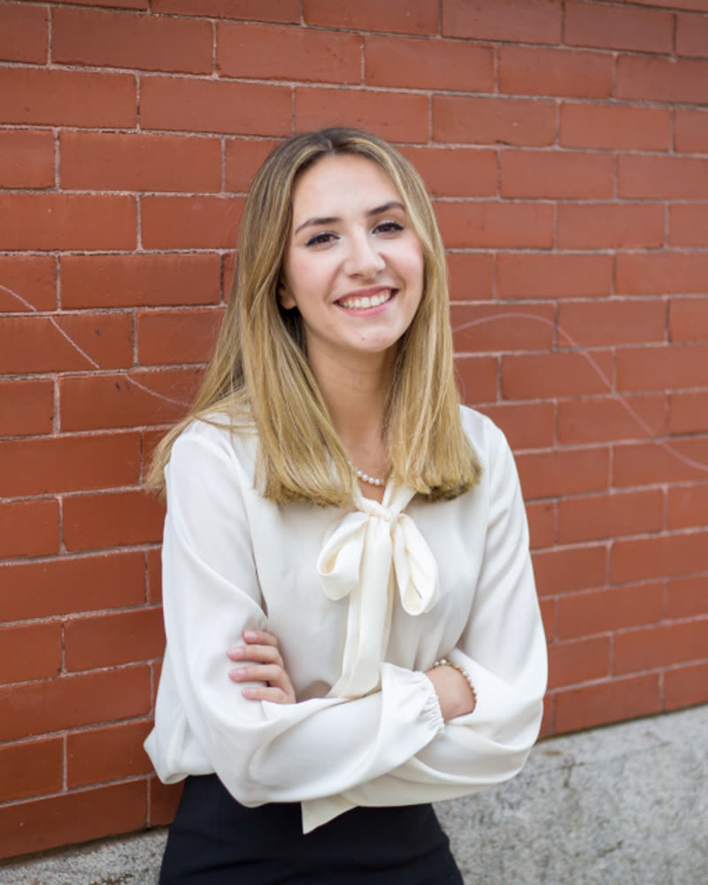 Portrait of Hannah Lindqvist, a smiling woman with long fair hair in a cream blouse in front of a brick wall