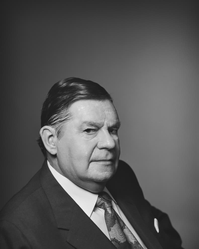 Black and white studio portrait of Gerald Halloran, an older man in a dark suit and patterned tie