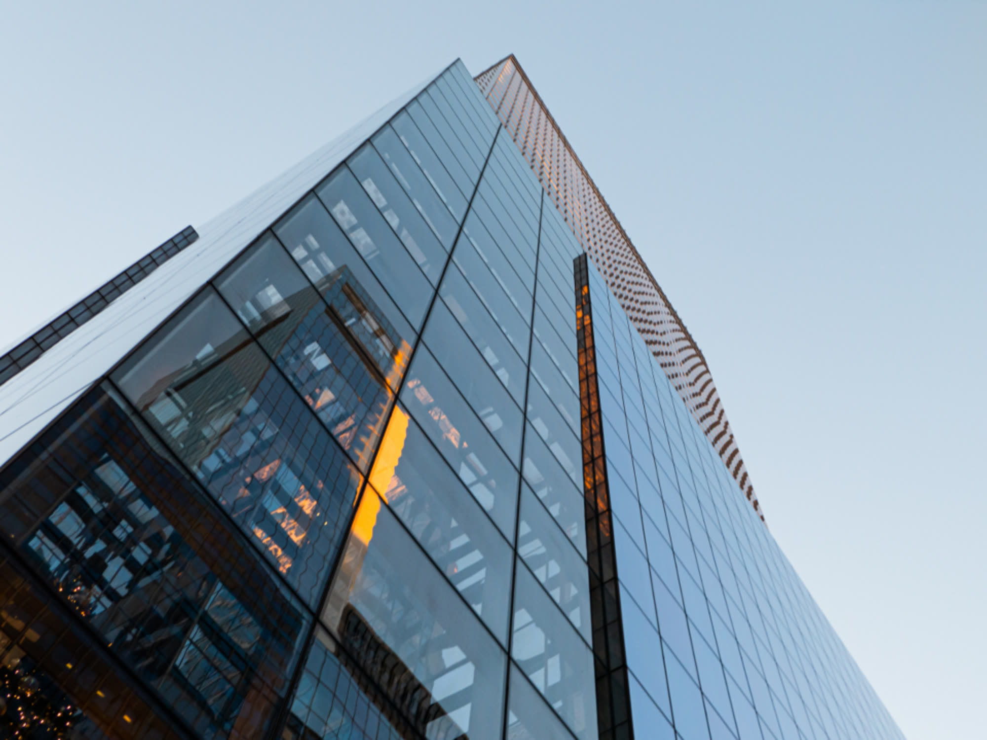 Looking up at a tall glass office tower against a pale sky